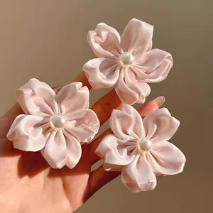 Détail de trois pinces à cheveux fleurs en satin rose avec perles centrales