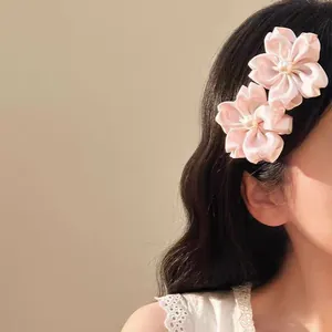 Gros plan de barrettes fleur de cerisier en satin rose avec perles sur cheveux ondulés