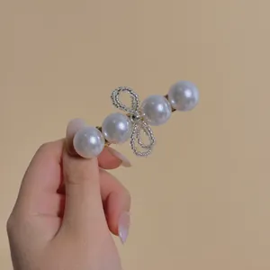 Elegant pearl hair clip with a beaded bow and gold finish on a warm background