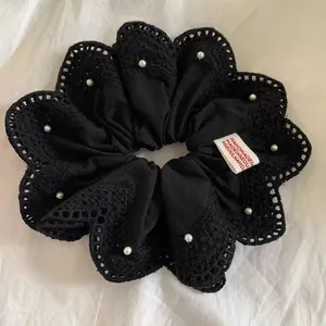 Detail van handgemaakte zwarte kant scrunchie met witte parels en gegolfde randen