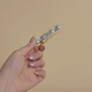 Elegant gold hair clip with large pearls and sparkling diamond heart held by hand