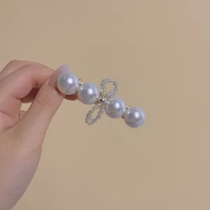 Elegant gold hair clip with four large white pearls and a beaded bow held by hand