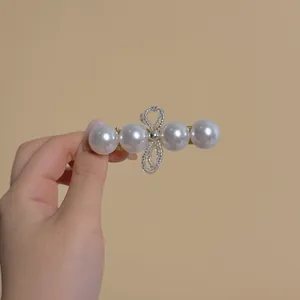 Close-up of a gold pearl hair clip with a delicate beaded bow on a warm beige backdrop