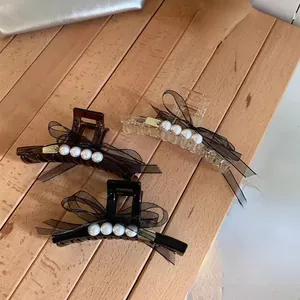 Drei elegante Haarklammern mit schwarzen Organzaschleifen und Perlen auf Holzgrund