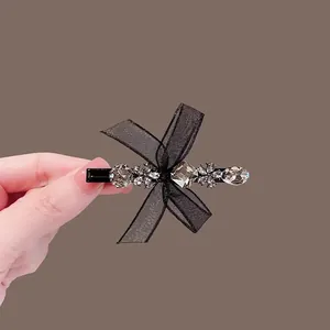 Elegant black lace bow hair clip with gray rhinestones held against a brown background