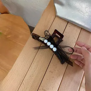 Große Haarspange mit schwarzer Organzaschleife und weißen Perlen auf Holztisch