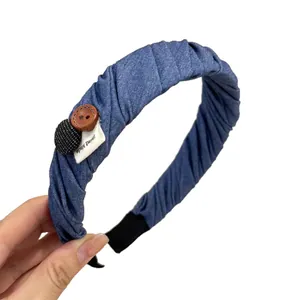 Blue denim fabric headband with handmade tag and dual buttons shown in a hand