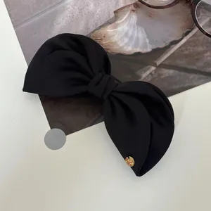 Elegant black fabric bow hair clip with gold metal logo detail on white surface