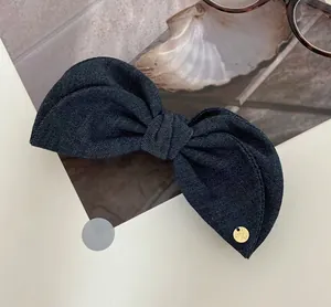 Close-up of dark denim bow hair clip with gold logo detail and fine fabric texture