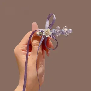 Eleganter lila Haarschleifenclip mit Kristallperlen und weißen Harzblüten in der Hand