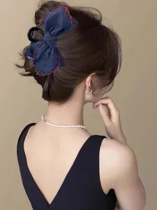 Detail of dark blue denim bow hair claw clip with red contrast stitching on model