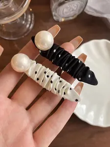 Detail showing a fabric hair clip with black and white polka dots and a large pearl bead
