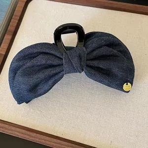 Retro denim blue bow hair claw clip with golden brand tag on textured fabric background