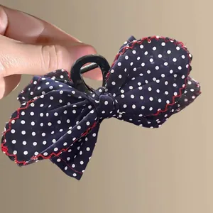 Navy blue polka dot bow hair claw clip with red stitching shown in hand close-up