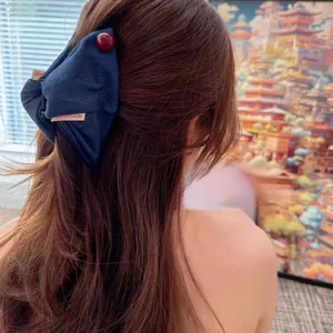 Detail of a navy blue denim bow hair claw with handmade label on long straight hair