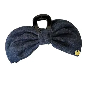 Vintage denim bow hair clip with dark blue fabric and a small gold metal logo pendant