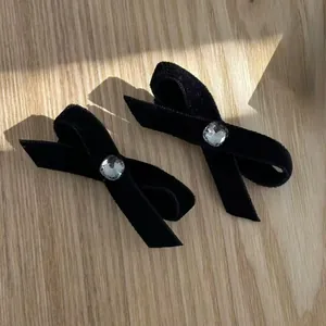 Paire de barrettes à cheveux en velours noir avec cristal central sur fond bois clair