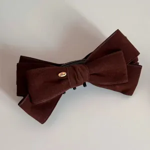 Macro shot of brown suede bow hair clip with gold Love charm and strong black grip