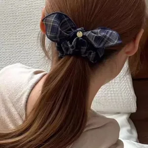 Classic dark blue plaid scrunchie with bow and gold charm worn on a low ponytail