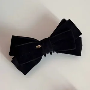 Close-up of a large black velvet bow hair clip with a golden Love metal logo