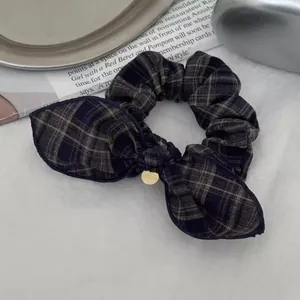 Detailed view of dark plaid bow scrunchie with a gold metal tag on a vintage background