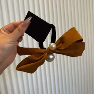 Detail of a brown suede bow hair tie with two pearl accents on high elastic black rubber band