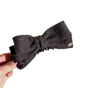Elegant wool fabric bow banana hair clip with gold logo detail on white background