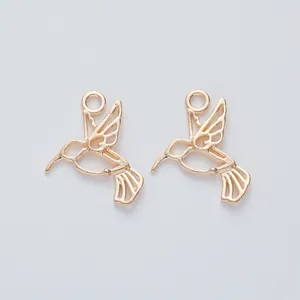 Detail view of two light gold hummingbird alloy pendants with intricate hollow design