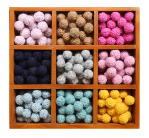 Colorful handmade wool felt pom pom balls in a nine-grid wooden tray for DIY crafts