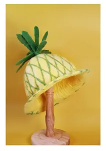 Close-up of handmade yellow wool felt pineapple hat with green leaf and grid texture
