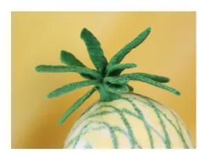 Macro detail of handmade wool felt pineapple hat showing green felt leaves and texture