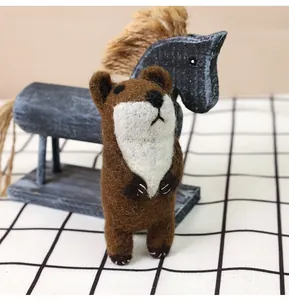 Detail of a handmade wool felt bear doll standing on a checkered cloth with a wooden horse