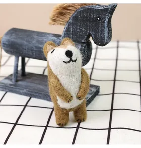 Handmade wool felt puppy figurine standing near a wooden rocking horse on plaid tablecloth