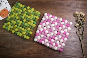 Close-up of square wool felt ball coasters in green and pink-purple tones on wood table