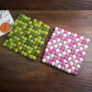 Handmade colorful square wool felt ball coaster and trivet on a vintage wood table