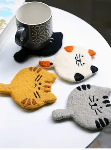 Close-up of four handmade wool felt cat coasters with cute ears and tails on a white table