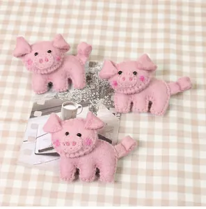Detailed view of three handmade pink wool felt pig brooches on a cozy plaid tablecloth