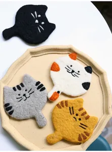 Detailed view of four assorted handmade wool felt cat coasters on a ceramic tray