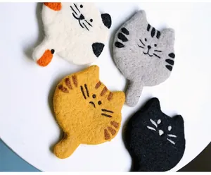 Detailed view of four handmade wool felt cat coasters with cute embroidered faces