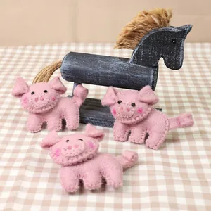Three handmade pink wool felt pig brooches on a rustic checkered tablecloth background