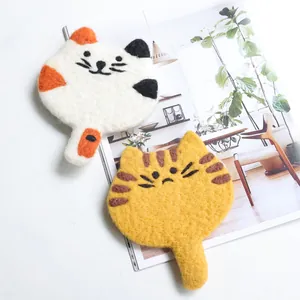 Handmade wool felt cat coasters set with calico and tabby patterns on a magazine