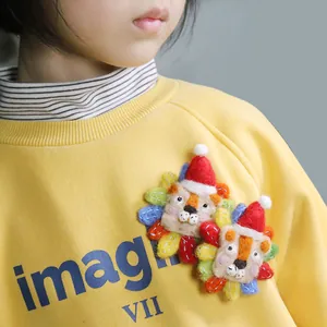 Handmade wool felt lion brooch with red Christmas hat on yellow sweater