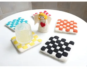 Close-up of checkered wool felt coasters in various colors with a glass on white desk
