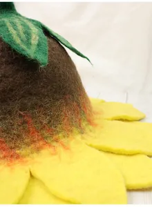 Detail view of handmade wool felt sunflower hat with yellow petals and brown core texture