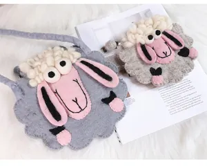 Détail d'un sac à bandoulière en laine feutrée en forme de mouton posé sur un tapis doux