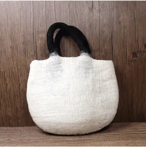 Close-up of minimalist off-white wool felt handbag with round black handles on wood surface