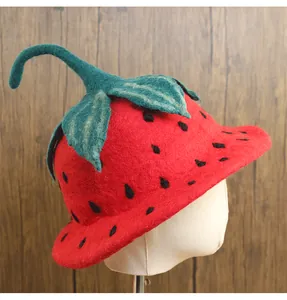 Dettaglio macro del cappello a fragola in feltro di lana rosso con stelo verde e semi