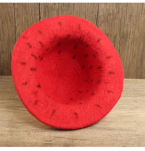 Dettaglio cappello fragola in feltro rosso con semi su sfondo di legno rustico