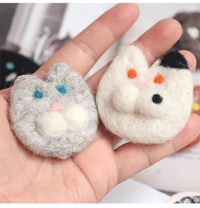 Close-up of handmade wool felt cat brooches in white and gray held in a palm