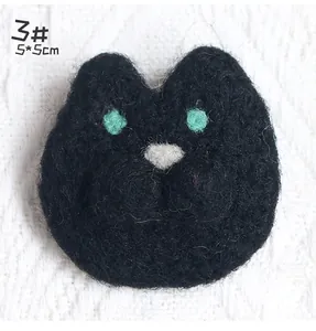 Macro shot of 5x5cm handmade black wool felt cat brooch with green eyes on knit background